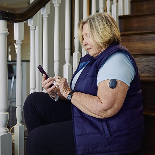 Kobieta, która siedzi na schodach i korzysta z aplikacji CGM Eversense razem z implantowalnym systemem CGM.